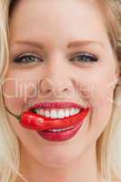 Cheerful blonde woman placing a chili between her teeth