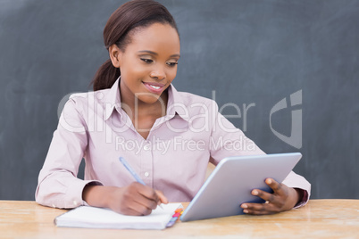 Teacher writing while looking at a tablet computer