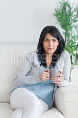 Woman relaxing on a sofa while holding a grey mug