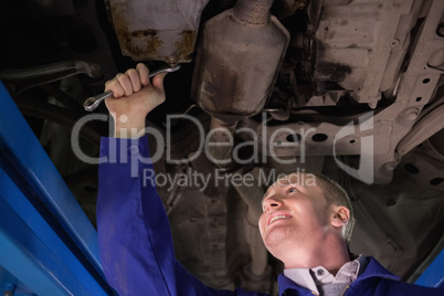 Smiling mechanic repairing the below of a car