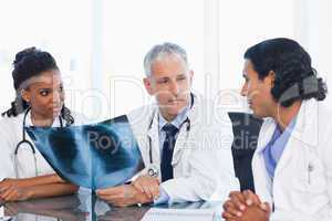 Mature doctor looking at an x-ray with two members of his team