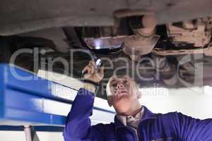 Mechanic looking at a car while holding a flashlight