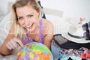 Beautiful woman with a suitcase pointing on a globe