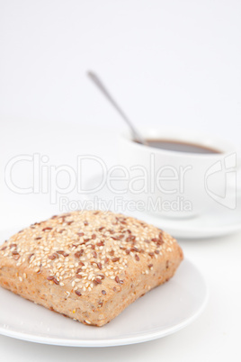Bread bun and a cup of coffee with a spoon on white plates