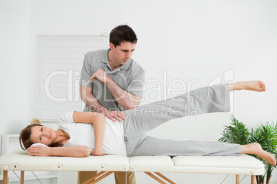 Doctor pressing his elbow on her hip while woman raising her leg