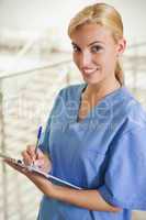 Nurse looking at camera while writing on a clipboard