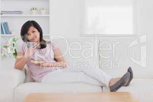 Woman sitting on a couch while holding a mug and a book