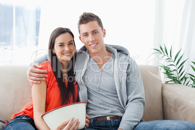 A smiling couple sitting on the couch look into the camera
