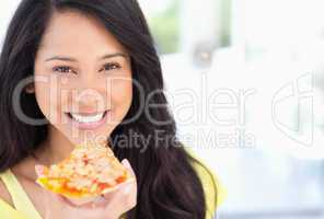 A smiling woman holding a slice of pizza as she looks at the cam