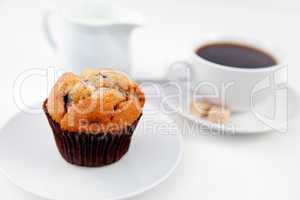 Muffin and a cup of coffee on white plates with sugar and milk