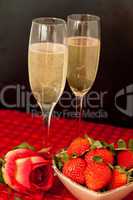 Top glasses of champagne with strawberries in a bowl and a rose