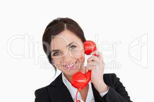 Smiling woman in suit using a red dial telephone