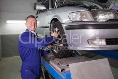 Smiling mechanic standing while repairing a car wheel