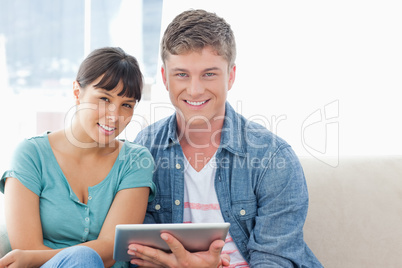 A smiling couple hold a tablet pc while looking at the camera