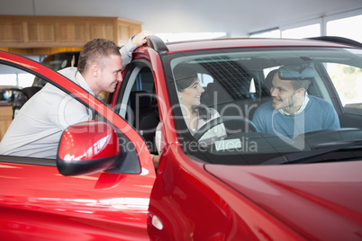 Couple listening to a salesman while sitting on a car