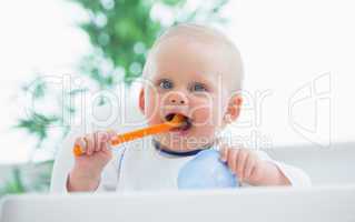 Baby looking at camera while holding a plastic spoon
