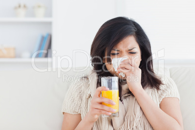 Sneezing woman drinking a glass of orange juice