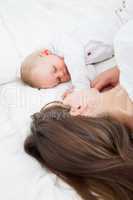 Brunette woman lying with her baby on her bed