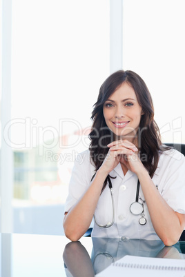 Smiling doctor sitting at the desk with her elbows on the table