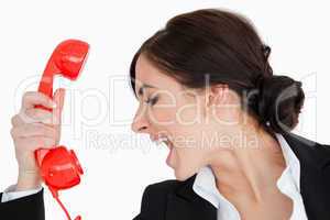 Woman in suit shouting against a red dial telephone