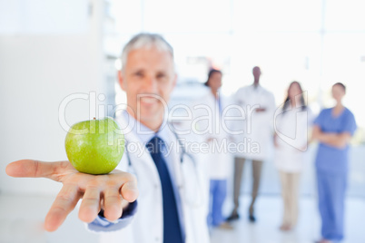 Green apple held by a doctor with a team behind him