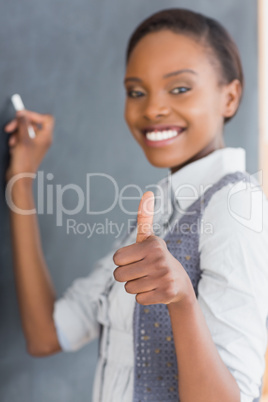 Teacher with thumb up writing on a blackboard