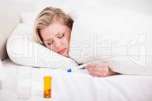 Sick blonde woman looking at her thermometer