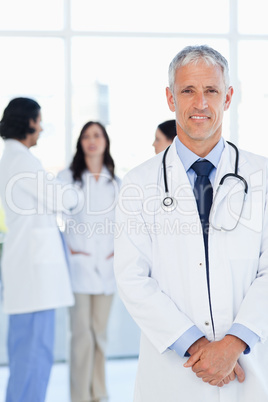 Doctor smiling while his team is communicating in the background