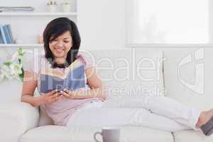 Woman reading a book while lying on a sofa