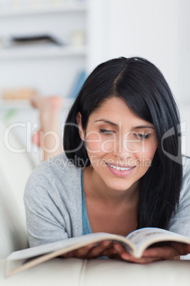Woman smiling as she reads a book while lying on a couch
