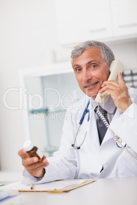 Doctor holding a drug box and a phone while sitting