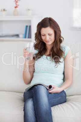 Woman holding a glass while reading a magazine