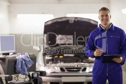 Smiling mechanic holding a clipboard next to a car Smiling mechanic holding a clipboard next to a car