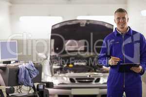 Smiling mechanic holding a clipboard next to a car