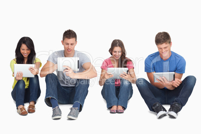 Four friends sitting on the ground all with tablets