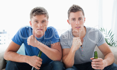 A pair of guys looking into the camera with beer in hand as they