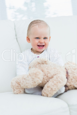 Baby smiling with teddy bear on his knees