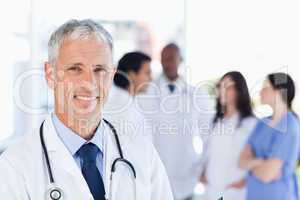 Mature doctor standing upright while waiting for his team