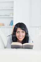 Woman holding a book while smiling and lying on a couch