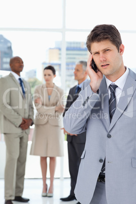 Serious businessman using a cell phone while his team is behind