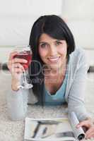 Woman smiling while holding a glass of wine and a magazine on th