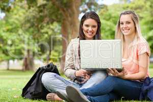 Smiling teenagers sitting while using a laptop