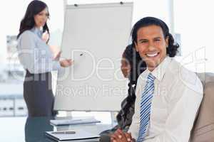 Young employee smiling during a presentation while his team is w