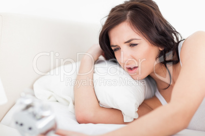 Brunette woman waking up while looking at her alarm clock