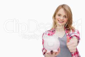 Woman with thumb up while holding a piggy bank