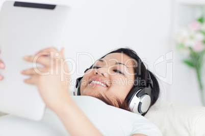 Smiling woman lying on a coach with headphones on and holding a