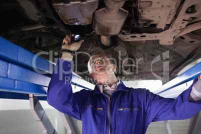 Mechanic looking the below of a car while holding a flashlight