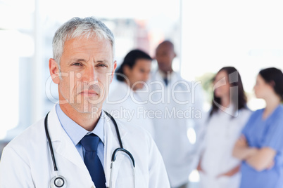 Mature doctor looking straight ahead while his team is looking a