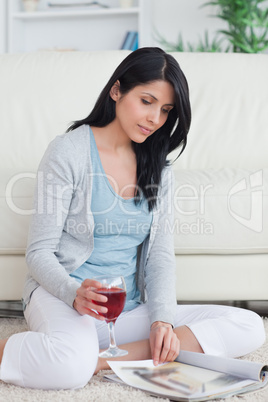 Woman holding a glass of red wine while turning pages of a magaz