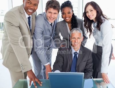 Mature manager sitting at the desk surrounded by his smiling bus